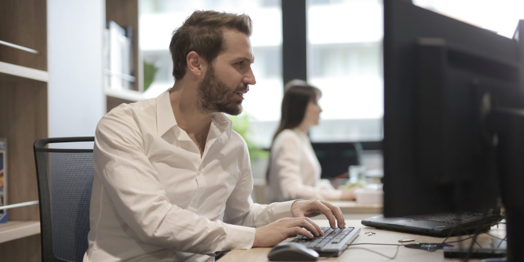 thoughtful-young-bearded-manager-typing-on-keyboard-while-3966786